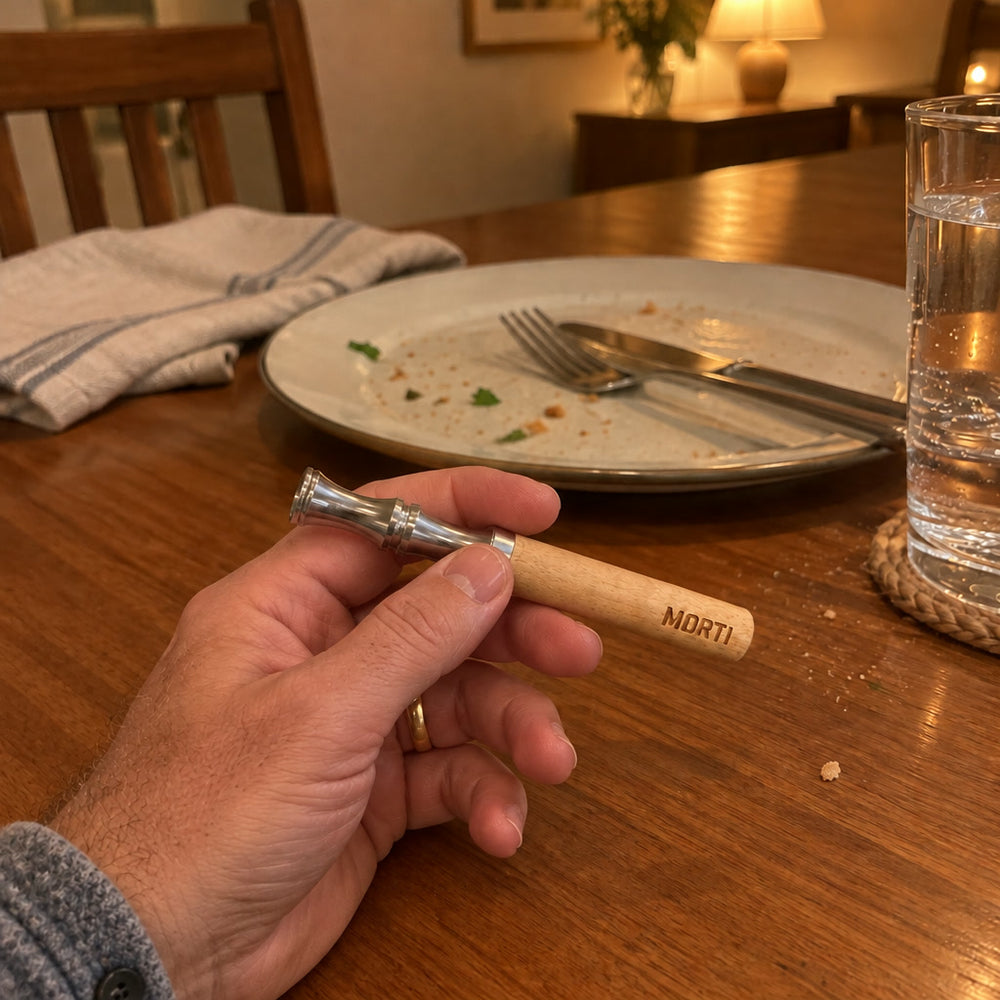 A man's hand holding the Morti pen at the dinner table after a meal